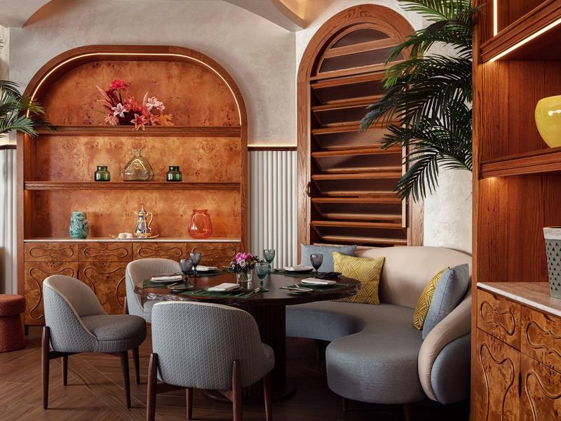 Elegantní jídelní prostor s kulatým stolem, čalouněnými židlemi a dekorativními rostlinami v teplé atmosféře