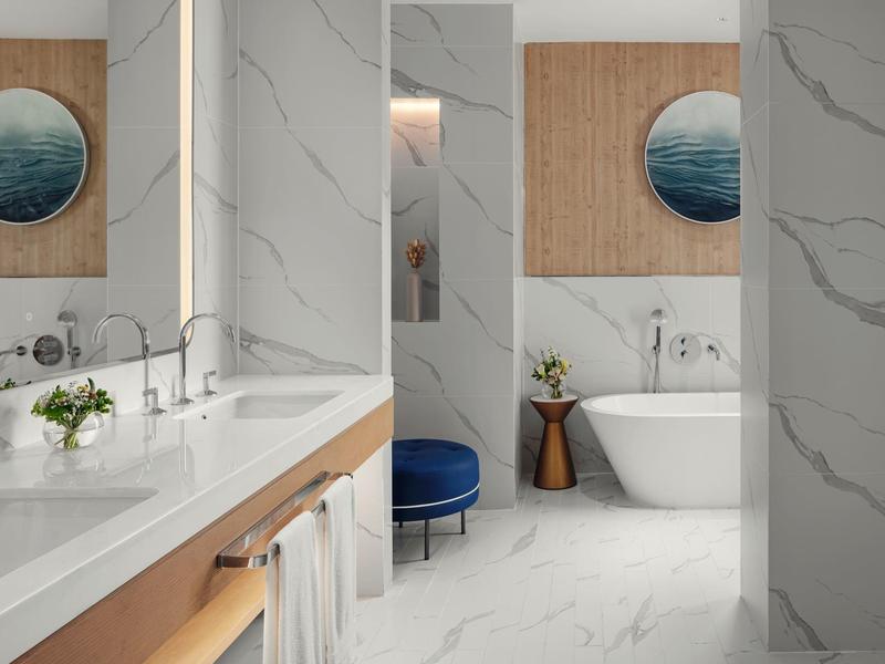 Moderní koupelna s bílým mramorem, volně stojící vanou a dřevěnými doplňky.