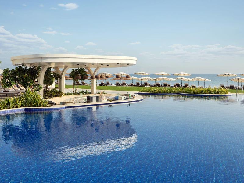 Velký venkovní bazén s barem u bazénu, slunečníky a výhledem na moře za jasného počasí
