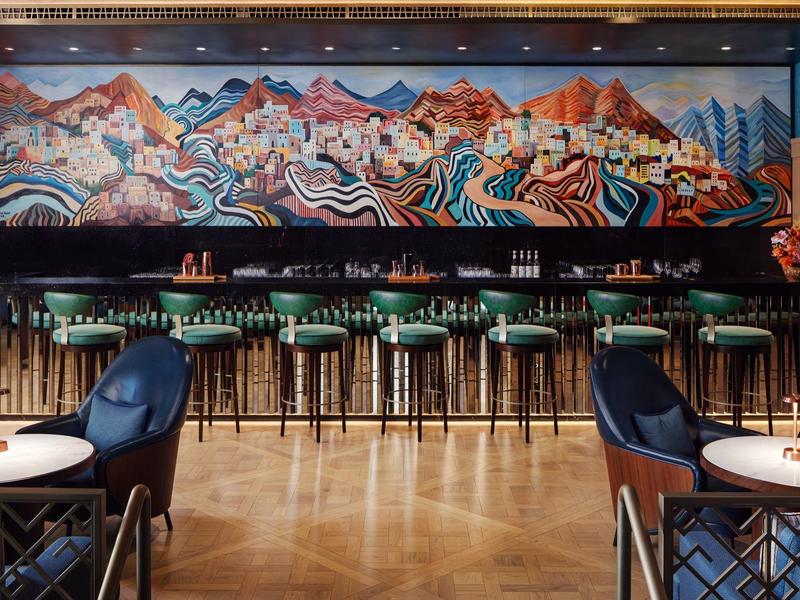 Bar s vysokými stoličkami a barevným freskovým malbám na pozadí v hotelu.
