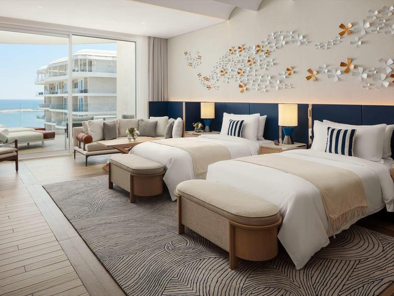 Moderní hotelový pokoj se dvěma postelemi, posezením a výhledem na moře přes velká okna.