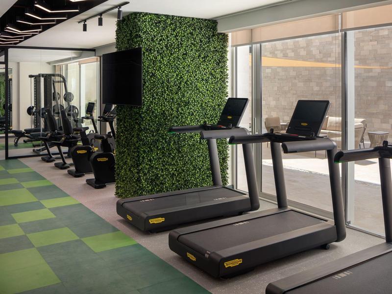 Moderní posilovna s běžeckými pásy, činkami a velkým oknem s výhledem ven.