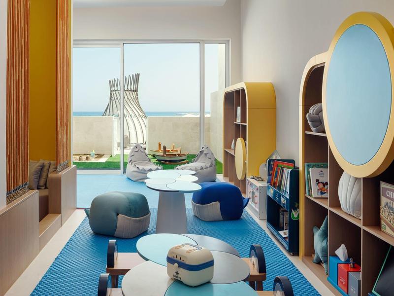 Moderní dětský herní koutek s barevnými sedacími pytli, stoly a regály v světlé místnosti.