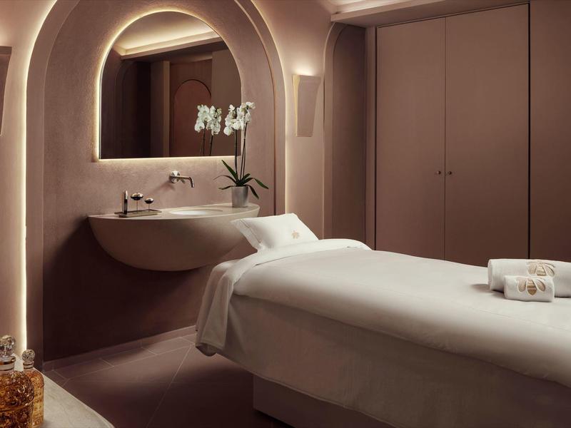 Elegantní masážní pokoj s pohodlným stolem, teplým osvětlením a stylovým zrcadlem.