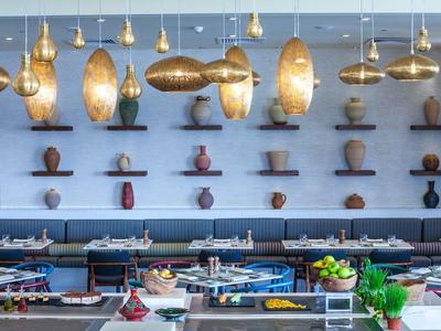 Moderní restaurace se závěsnými zlatými lampami a dekorativními vázičkami na zdi.