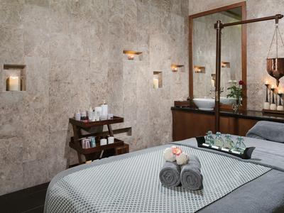 Gemütlicher Wellnessraum mit Massageliege, Handtüchern, Kerzen und natürlichen Wandnischen.