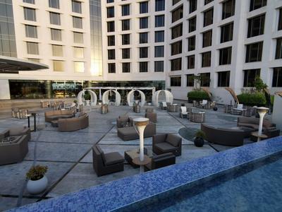 Moderner Außenbereich mit grauen Sitzmöbeln, runden Pavillons und hohem, weißem Hotelgebäude.