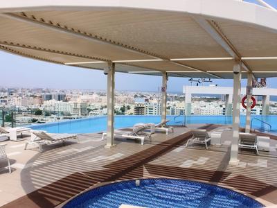 Střešní terasa s bazénem a vířivkou, výhled na město a moře pod slunečníkem.