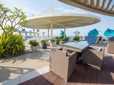 Moderne Terrasse mit braunen Sesseln, Pflanzen und blauen Sonnenschirmen neben Meerblick.