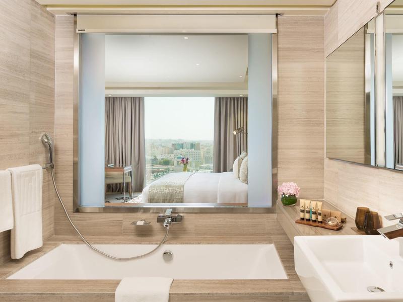 Modernes Badezimmer mit Badewanne, großem Spiegel und weißem Waschbecken, Blick ins Schlafzimmer.