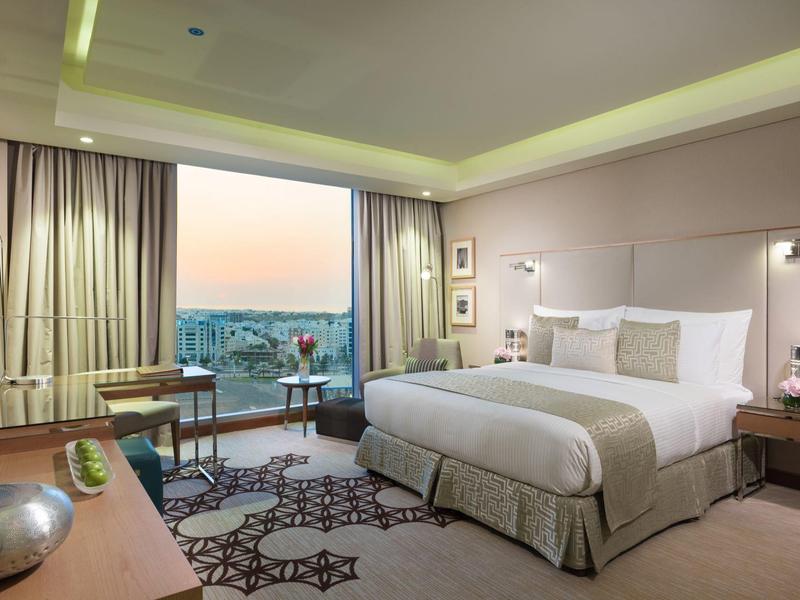 Modernes Hotelzimmer mit großem Bett, Panoramafenster und stilvoller Einrichtung in neutralen Tönen.