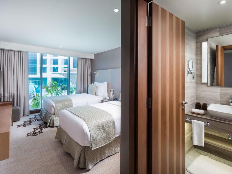 Modernes Hotelzimmer mit zwei Betten, großem Fenster, Vorhängen und angrenzendem Badezimmer.