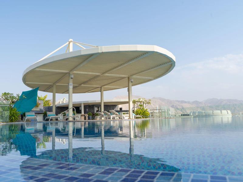 Großer Pool mit rundem, weißem Sonnendach und klarer Spiegelung bei klarem Himmel.