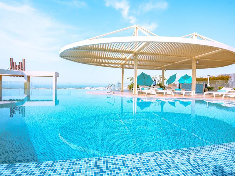Infinity-Pool mit runder Überdachung, blauen Liegestühlen und Meerblick unter blauem Himmel.