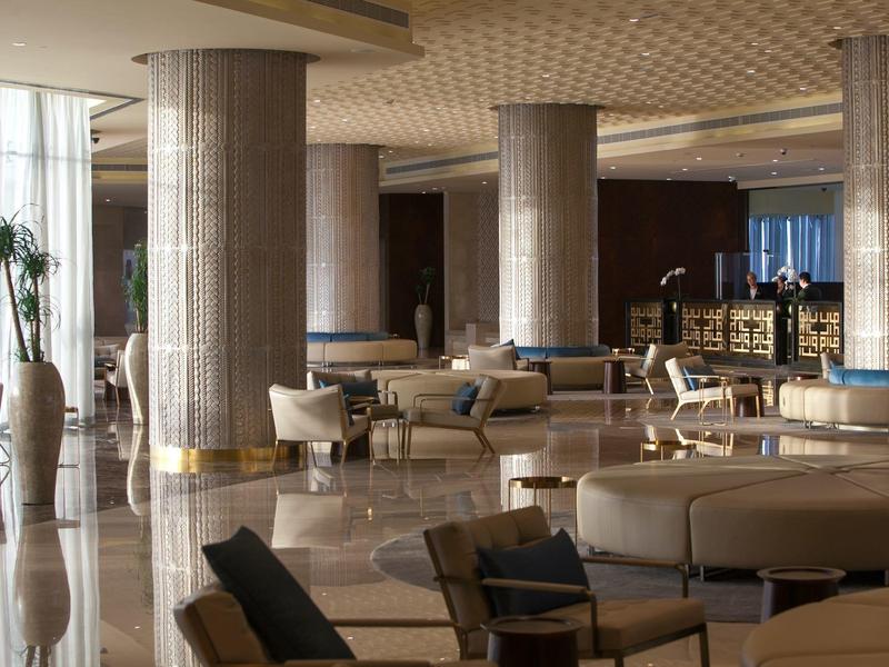 Großer, heller Hotel-Lobbybereich mit Säulen, Sesseln, Sofas und Pflanzen, modern und einladend gestaltet.