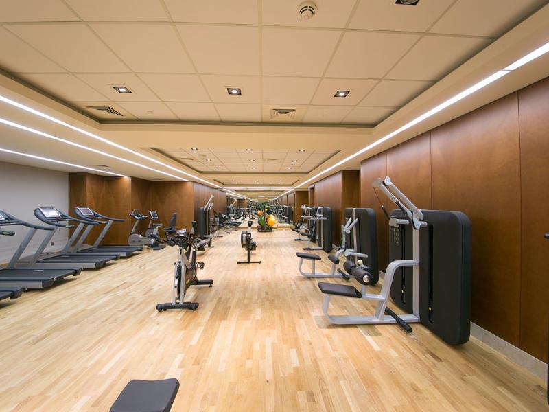 Moderner Fitnessraum mit Holzfußboden, Laufbändern, Trainingsgeräten und braunen Wänden.