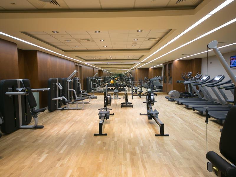 Großer Fitnessraum mit Holzfußboden, Gewichten, Laufbändern und Spiegelflächen an den Wänden.