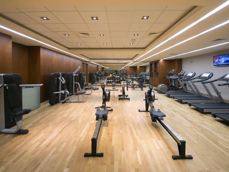 Moderner Fitnessraum mit Rudergeräten, Laufbändern und Holzboden, Wände in warmem Braunton.