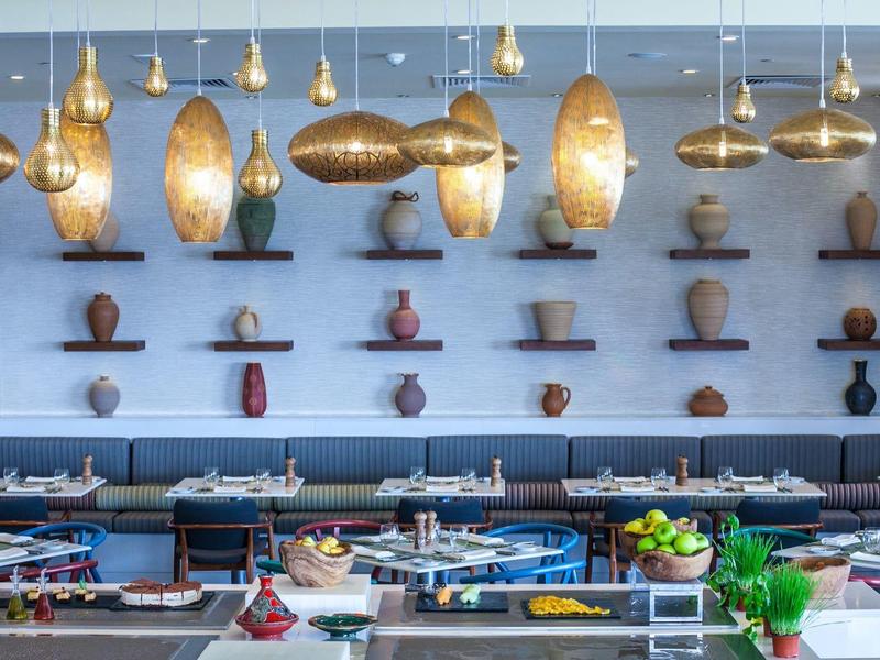 Modernes Restaurantinterieur mit blauen Wänden, hängenden goldfarbenen Lampen und dekorativen Vasen.