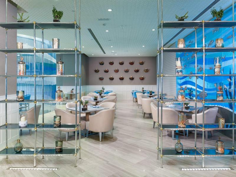 Moderner Gastraum mit Glasregalen, runden Sesseln und blauen Wanddekorationen.