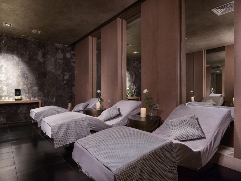 Dunkler Wellnessraum mit drei weißen Liegen, warmem Licht und entspannender Atmosphäre.