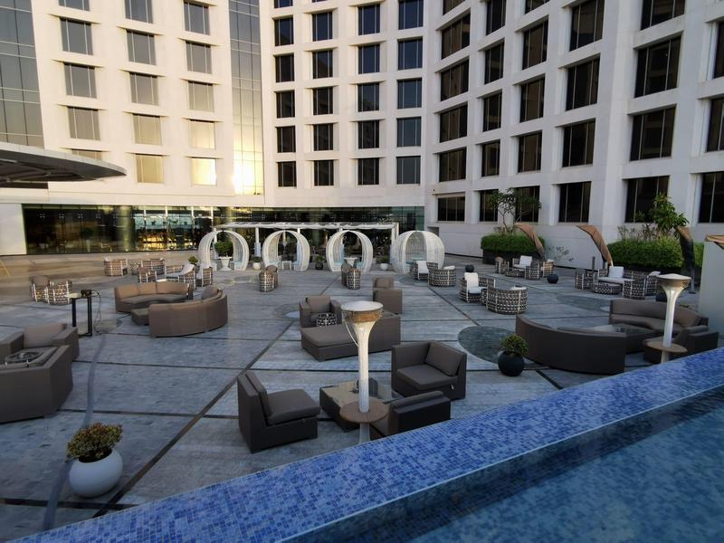 Moderner Außenbereich mit grauen Sitzmöbeln, runden Pavillons und hohem, weißem Hotelgebäude.