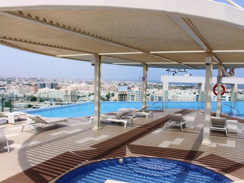 Dachterrasse mit Pool, Sonnenschirm, Liegestühlen und Blick auf Stadt und Meer am Horizont.
