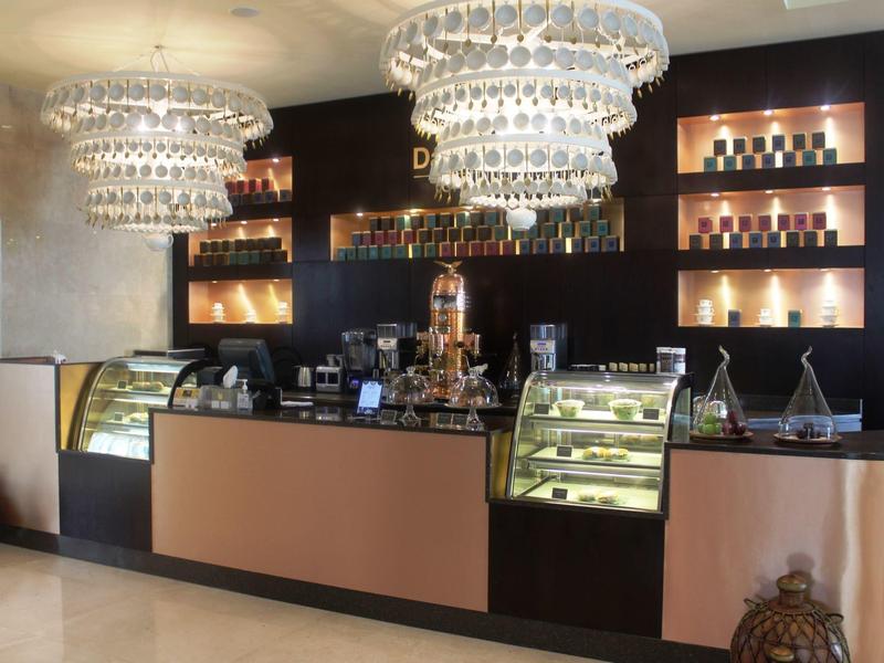 Moderner Café-Tresen mit goldfarbenen Vitrinen, zwei großen Kronleuchtern und Regalen mit Flaschen.