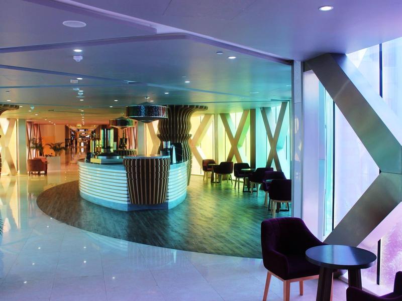 Moderner Hotel-Lobby mit rundem Empfangstresen, Holzfußboden und farbig beleuchteten Wänden.