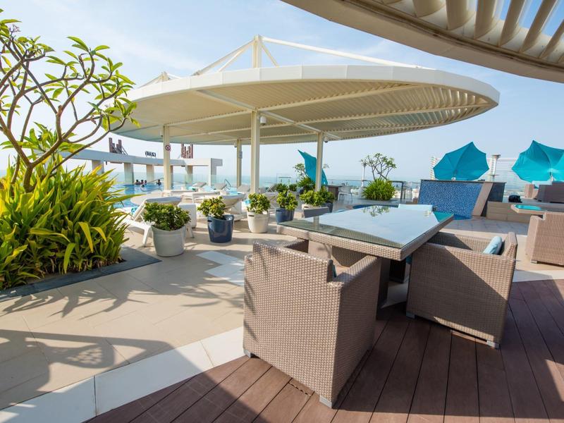 Moderne Terrasse mit braunen Sesseln, Pflanzen und blauen Sonnenschirmen neben Meerblick.