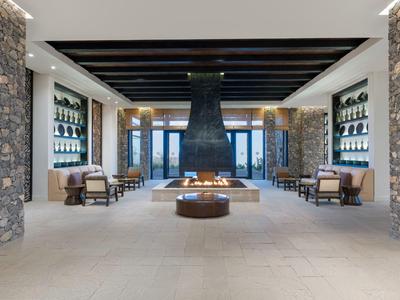 Spacious hotel lobby with modern furniture and central fireplace between stone pillars.