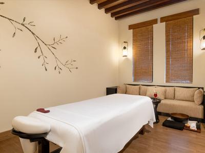 Calm massage room with wooden beam ceiling, comfortable table, and cozy seating area.