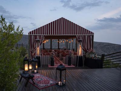 Gemütlicher, beleuchteter Zeltpavillon mit weichen Sitzgelegenheiten auf einer Holzterrasse bei Dämmerung.