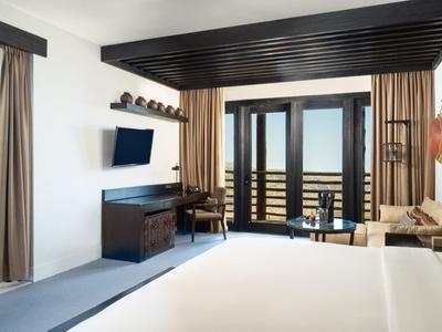 Modern hotel room with large bed, TV, balcony with sea view, and adjacent bedroom.
