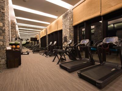 Moderner Fitnessraum mit Laufbändern und Steinwänden in einem Hotel.