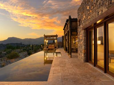 Moderner Steinhaus mit Infinity-Pool und Bergblick bei Sonnenuntergang.