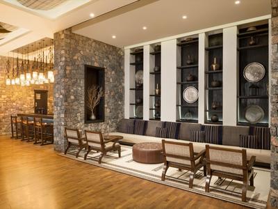 Modern hotel lounge area with chairs, sofa, and wall shelving with decorations.