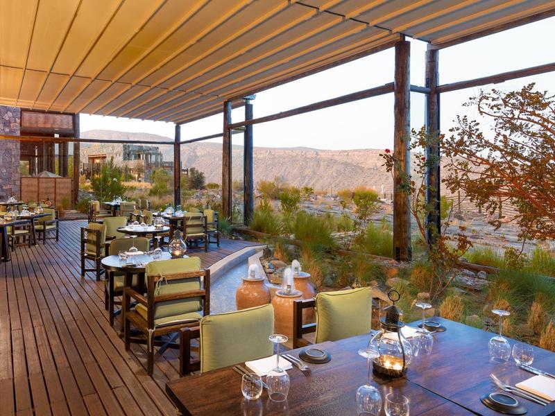 Covered terrace with set tables and a view of a landscape at sunset.