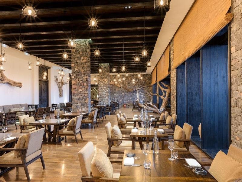Modern restaurant with wooden tables, comfortable chairs, and stone walls in a hotel.