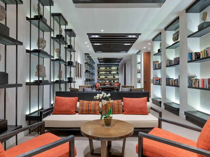 Modern hotel lounge area with orange armchairs and bookshelves on the walls.