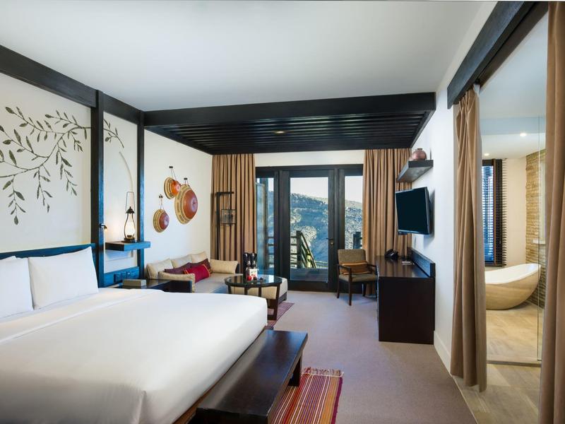 Modern hotel room with large bed and mountain view.