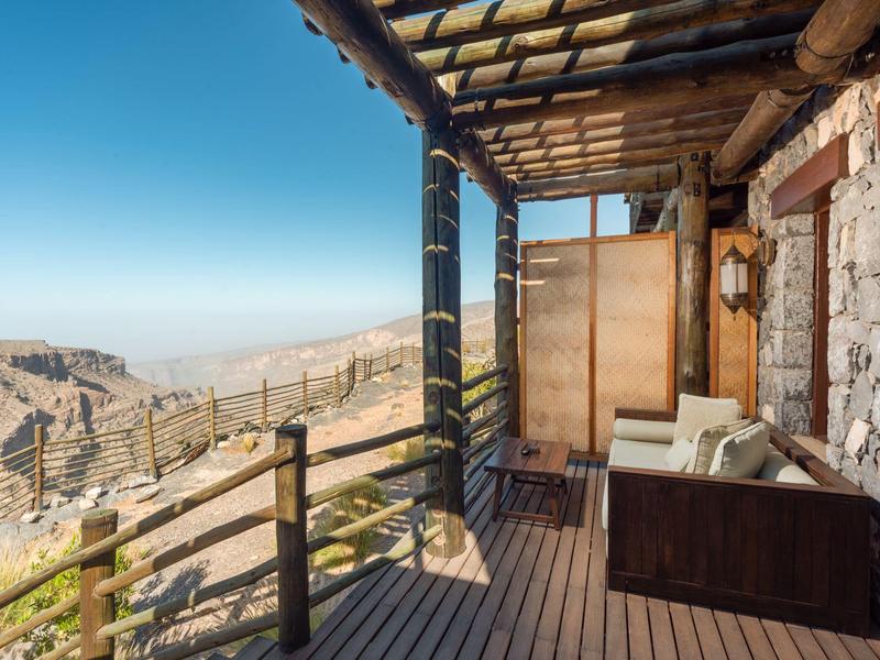 Balcony with wooden floor and sofa overlooking mountain landscape and clear sky.