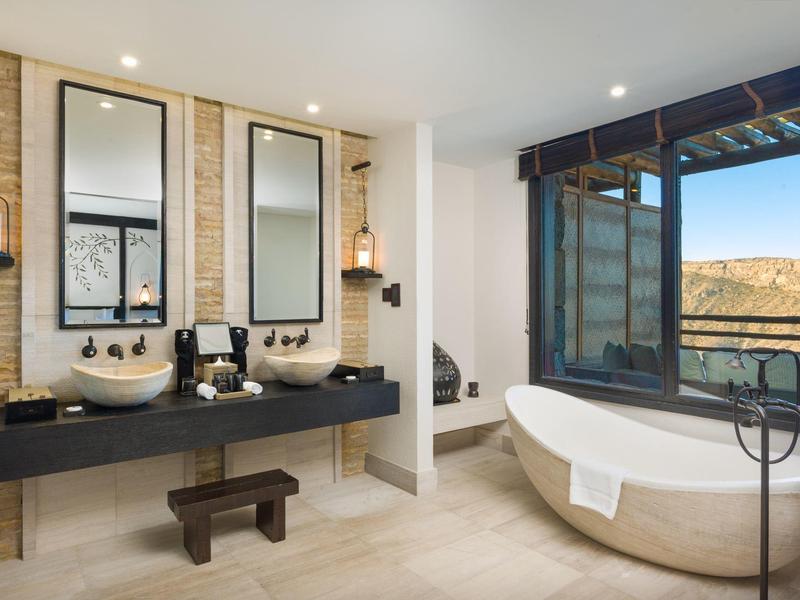 Modern bathroom with two sinks, freestanding bathtub, and large window with a view.