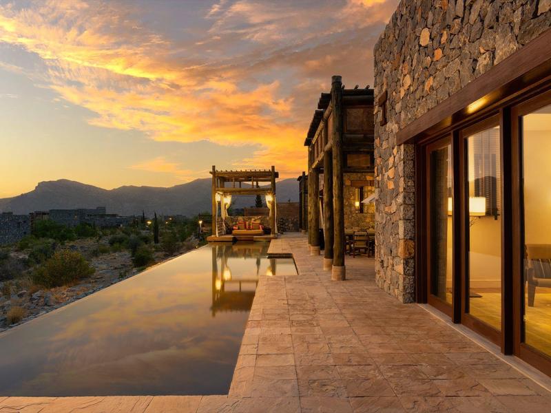 Modern stone house with pool overlooking mountain landscape at sunset.