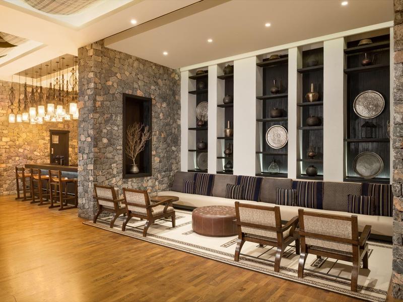 Modern hotel lounge area with chairs, sofa, and wall shelving with decorations.