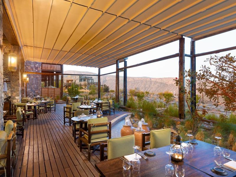 Outdoor restaurant area with wooden flooring, set tables, and mountain view at sunset.