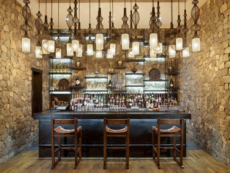 Rustic hotel bar with stone walls, wooden bar stools, and numerous pendant lights.