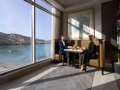 Due persone sedute in un ristorante con grandi vetrate che si affacciano sul mare.