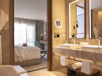 Modern hotelkamer met open badkamer, dubbele wastafels en zicht op de slaapkamer.