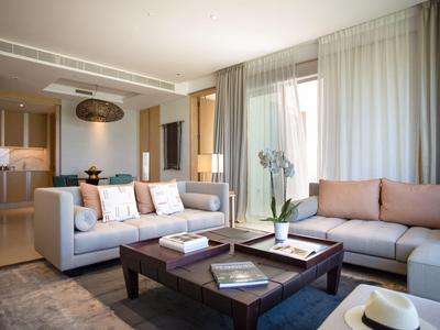 Moderne woonkamer met twee lichte banken, een donkerhouten salontafel en doorschijnende gordijnen.